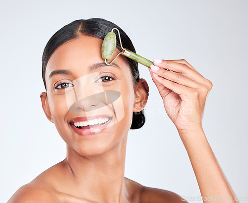 Image of Portrait, beauty and facial massage roller with a woman in studio on a white background holding a stone. Face, smile and skincare with a happy young model looking confident at luxury wellness