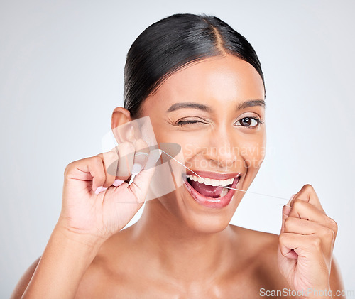 Image of Woman, portrait and wink to floss teeth in studio for healthy dental care, gum gingivitis or plaque on white background. Face, happy indian model and oral thread for cleaning mouth, tooth and hygiene