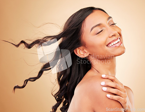 Image of Curly hair, smile and woman in wind at studio isolated on a brown background. Hairstyle breeze, natural cosmetics and happy Indian model in salon treatment for beauty care, hairdresser and balayage