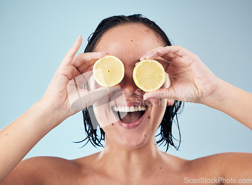 Image of Eyes, smile or happy woman with lemon for skincare or beauty in studio on blue background. Crazy, dermatology shine or funny person with natural fruits, vitamin c or face glow for wellness or health