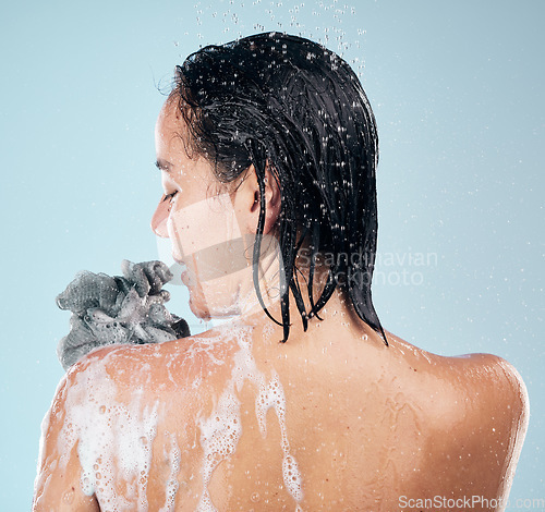 Image of Woman, back and cleaning body with water, soap and sponge for dermatology, skincare and blue background in studio. Person, smile and washing skin with self care, cosmetics or peace in bathroom