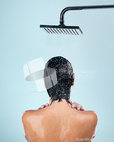 Image of Woman, shower and back in water drops for washing, grooming or hygiene against a blue studio background. Rear view of female person in body wash, cleaning or skincare routine under rain in bathroom