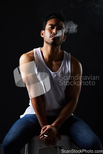 Image of Smoking portrait, sexy man and chair in studio in fitness, beauty aesthetic and strong sensual fashion. Art, body and male model with muscle, cigarette and jeans on black background in dark lighting.