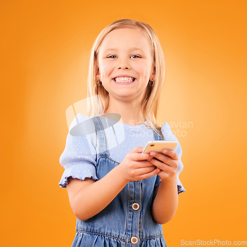 Image of Child, portrait and typing with smartphone in studio for social media, play mobile games and smile on orange background. Happy girl kid, phone and reading notification, watch multimedia and tech app