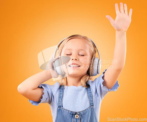 Image of Headphones, happy or child streaming music to relax with freedom in studio on orange background. Hand up, singing or girl singer listening to a radio song, sound or gospel on an online subscription