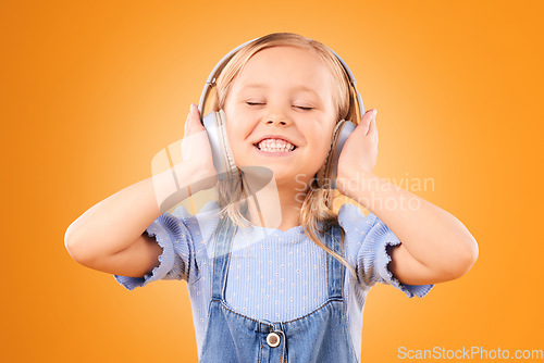 Image of Headphones, smile or child streaming music to relax with freedom in studio on orange background. Face, singing or happy girl singer listening to a radio song, sound or audio on an online subscription