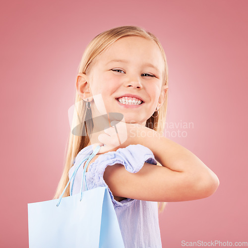 Image of Portrait, girl kid with shopping bag or gift, customer and purchase with fashion or birthday party on pink background. Retail, smile and child with present, luxury and event with happiness in studio