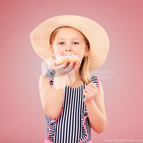 Image of Girl kid, eating a donut and dessert, sweets and summer with hat and bathing suit isolated on pink background. Portrait, youth and cake with snack, child enjoying bakery treat with hat in studio