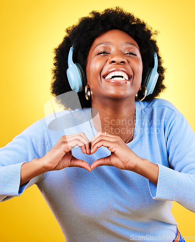 Image of Portrait, heart hands and headphones of woman in studio for sign, kindness or thank you on yellow background. Happy african model, finger shape or icon of hope, love or emoji while listening to music