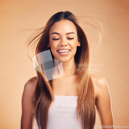 Image of Face, hair and wind with an aesthetic woman in studio on a brown background for shampoo treatment. Smile, beauty and keratin with a happy young model at the salon for growth or natural haircare
