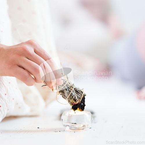 Image of Woman lighting a smudge kit with herbal stick. Natural elements for cleansing environment from negative energy, adding positive vibes. Spriritual wellness practices.