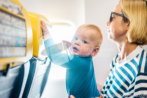 Image of Mom and child flying by plane. Mother holding and playing with her infant baby boy child in her lap during economy comercial flight. Concept photo of air travel with baby. Real people.