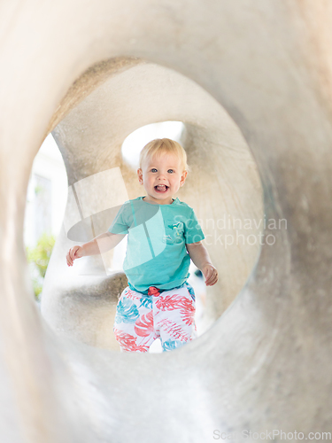 Image of Child playing on outdoor playground. Toddler plays on school or kindergarten yard. Active kid on stone sculpured slide. Healthy summer activity for children. Little boy climbing outdoors.