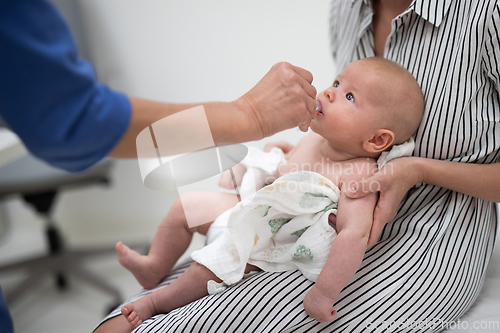 Image of Pediatrician administring oral vaccination against rotavirus infection to little baby in presence of his mother. Children health care and disease prevention