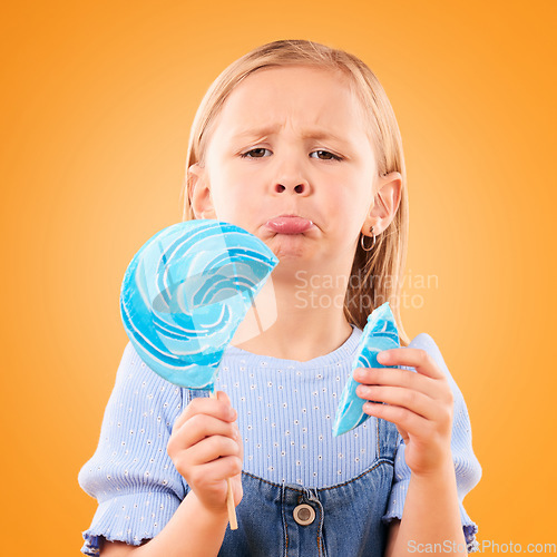 Image of Portrait, children and sad girl with a broken lollipop on an orange background in studio looking upset. Kids, candy and unhappy with a female child holding a cracked piece of a sugar snack in regret