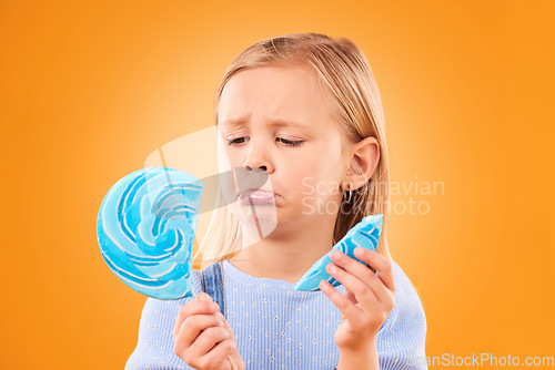 Image of Children, candy and a sad girl with a broken lollipop on an orange background in studio looking upset. Kids, sweets and unhappy with a female child holding a cracked piece of a sugar snack in regret