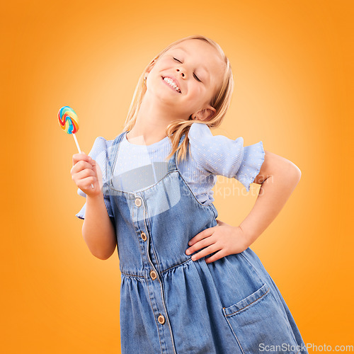 Image of Happy, lollipop and girl child with candy, hungry for dessert .and isolated on an orange background in studio. Smile, sweets and young kid with sugar, unhealthy food and eating confectionery treats