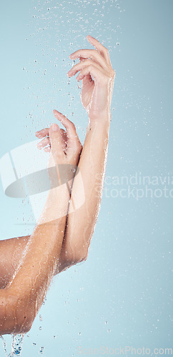 Image of Water drops, hands and person closeup with cleaning, shower and morning dermatology in studio. Blue background, arm and splash for wellness, washing and skin glow with self care and hygiene safety