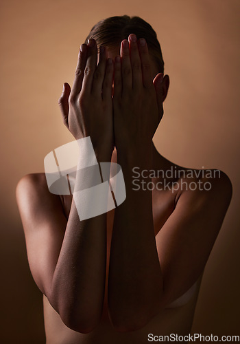 Image of Woman, body and hands covering face on dark brown background in studio for creative aesthetic, art deco and skin texture. Shy person, model and hide in shadow for nude beauty, wellness and sensuality