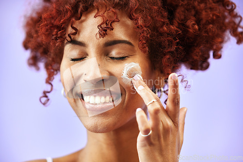 Image of Beauty, skincare or happy woman with face lotion or sunscreen creme product in grooming routine. Dermatology cosmetics, purple background or biracial model with smile to apply facial cream in studio