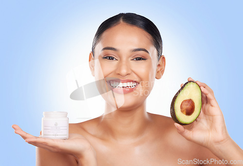 Image of Woman, cream and avocado with natural beauty, vegan product and sustainable skincare on blue background. Portrait, smile and green fruit, lotion and eco friendly skincare with glow in a studio