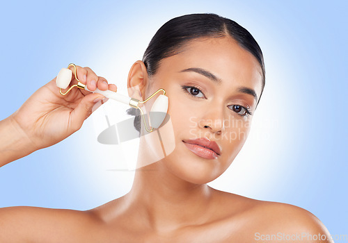 Image of Woman, face and roller, beauty and skincare with tools, stone and natural cosmetics on blue background. Facial massage, portrait and skin glow, crystal and equipment with dermatology in a studio