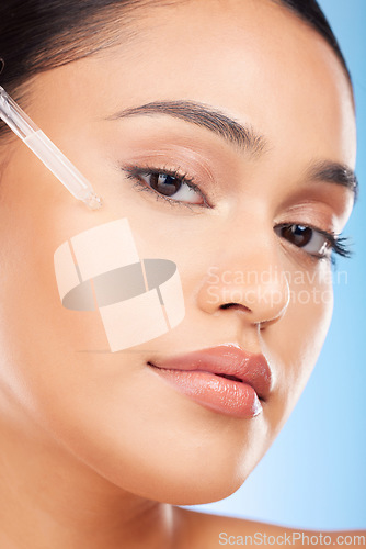 Image of Woman, portrait and essential oil for beauty, skincare and cosmetics product on a blue background. Young person with facial serum, dermatology dropper or collagen for skin care on face in studio