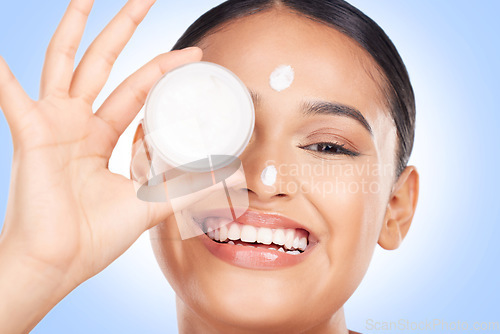 Image of Portrait, happy woman and cream container for face, aesthetic skincare and shine on blue background. Young model, facial beauty and moisturizer jar for sunscreen, cosmetics and dermatology in studio