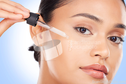 Image of Woman, portrait and oil serum for beauty, cosmetics and skincare product on a blue background. Young person with facial liquid, dermatology dropper or collagen for skin care makeup on face in studio