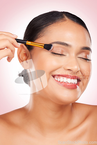 Image of Happy, eyeshadow and a woman with a brush on a pink background for skincare, wellness and health. Smile, young and a female model with makeup, beauty or foundation on face for cosmetics on a backdrop