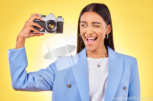 Image of Camera, photography and woman picture with a smile and wink for job in studio. Happy, young female person and yellow background with creative, memory and funny emoji face with photographer skill