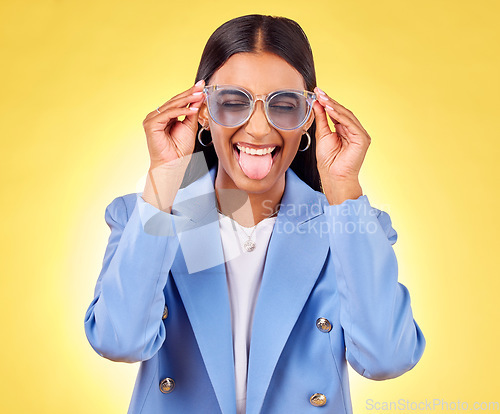 Image of Funny, woman smile and sunglasses with tongue out, comedy and silly face in a studio. Yellow background, crazy and female person with modern fashion, trendy cool style and creative work clothing