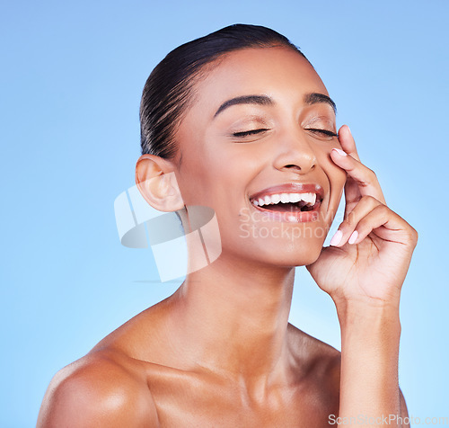 Image of Skincare, beauty and hand on face with happy woman in studio with blue background and dermatology or cosmetics. Indian, model and happiness with natural skin and healthy glow from facial or self care