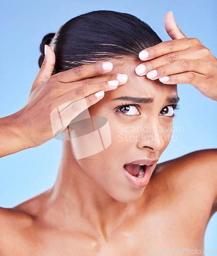 Image of Shock, pimple and young woman in studio for cosmetic, beauty and natural face routine. Health, wellness and Indian female model with acne skin on forehead for facial dermatology by a blue background.