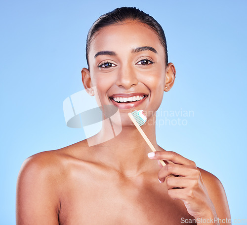 Image of Portrait, happy woman and brushing teeth on blue background for dental wellness, care and healthy smile in studio. Indian model, bamboo toothbrush and cleaning mouth for oral hygiene of fresh breath