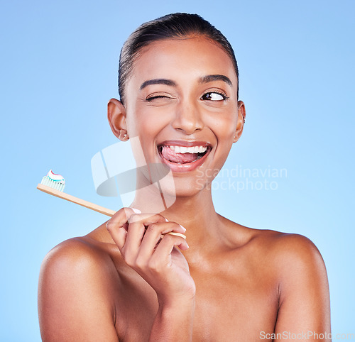 Image of Fun, woman or brushing teeth in studio for dental wellness, care or smile on blue background. Happy indian model, bamboo toothbrush or cleaning mouth for fresh breath, oral hygiene or tongue out wink