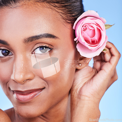 Image of Rose, portrait and skincare of woman in studio for eco cosmetics, natural glow and aesthetic on blue background. Face, happy indian model and flowers for beauty, sustainability or floral dermatology