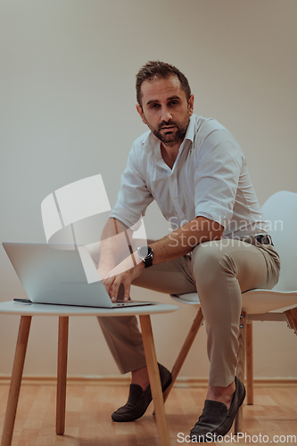 Image of A confident businessman sitting and using laptop with a determined expression, while a beige background enhances the professional atmosphere, showcasing his productivity and expertise.