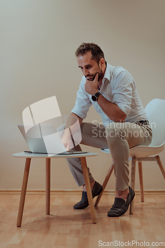 Image of A confident businessman sitting and using laptop with a determined expression, while a beige background enhances the professional atmosphere, showcasing his productivity and expertise.