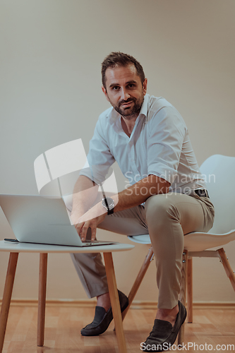 Image of A confident businessman sitting and using laptop with a determined expression, while a beige background enhances the professional atmosphere, showcasing his productivity and expertise.