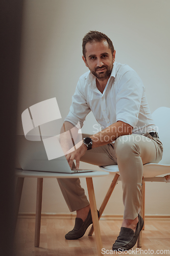 Image of A confident businessman sitting and using laptop with a determined expression, while a beige background enhances the professional atmosphere, showcasing his productivity and expertise.