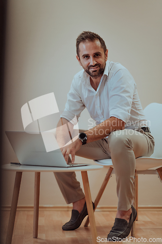 Image of A confident businessman sitting and using laptop with a determined expression, while a beige background enhances the professional atmosphere, showcasing his productivity and expertise.