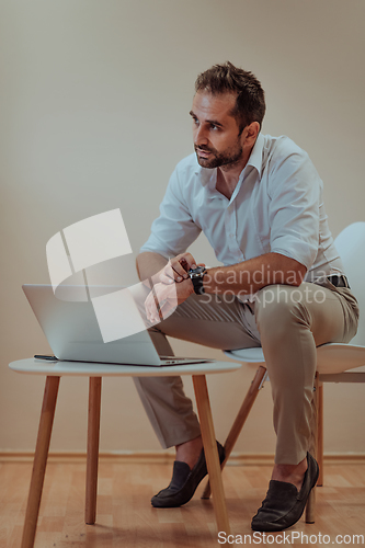 Image of A confident businessman sitting and using laptop and smartwatch with a determined expression, while a beige background enhances the professional atmosphere, showcasing his productivity and expertise.