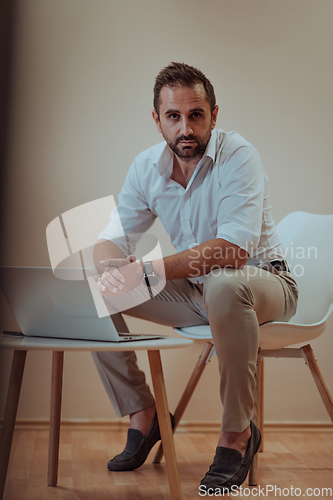 Image of A confident businessman sitting and using laptop with a determined expression, while a beige background enhances the professional atmosphere, showcasing his productivity and expertise.