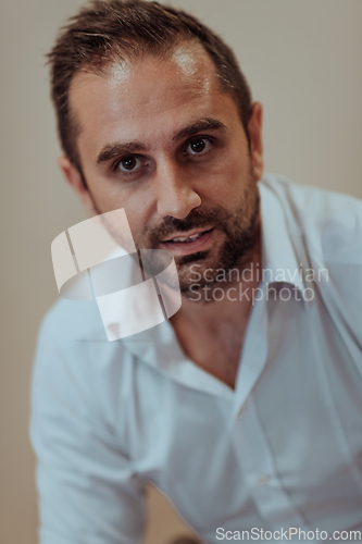 Image of A confident businessman sitting while a beige background enhances the professional atmosphere, showcasing his productivity and expertise.