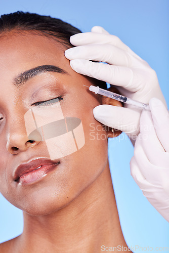 Image of Needle, woman and face on blue background for beauty, skincare process and aesthetic filler in studio. Indian model, hands of surgeon and injection for plastic surgery, facial change or prp cosmetics