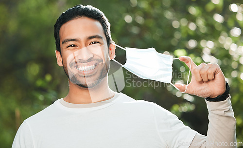 Image of Portrait, mask and remove with a man breathing fresh air in nature, feeling happy at the end of restrictions. Covid, freedom and smile for post lockdown with a young person in the forest or woods