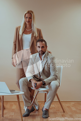 Image of A business couple posing for a photograph together against a beige backdrop, capturing their professional partnership and creating a timeless image of unity and success.