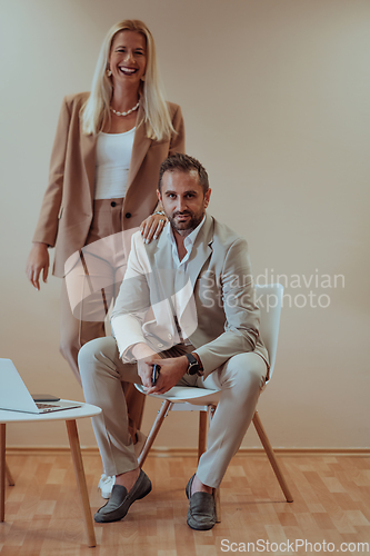 Image of A business couple posing for a photograph together against a beige backdrop, capturing their professional partnership and creating a timeless image of unity and success.