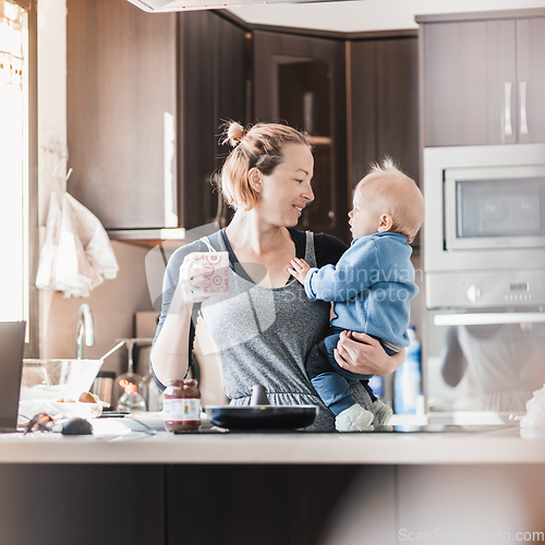 Image of Happy mother and little infant baby boy together making pancakes for breakfast in domestic kitchen. Family, lifestyle, domestic life, food, healthy eating and people concept.